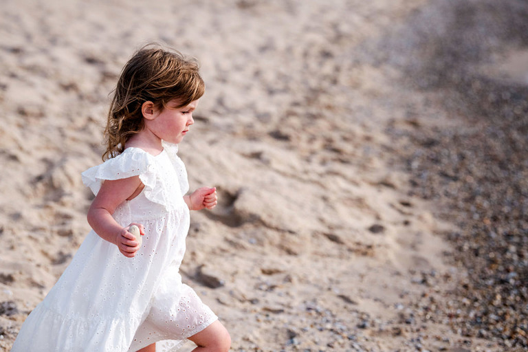 a little girl in a white dress holds a rock and is striding purposefully on the shore of Van's beach in Leland, MI.