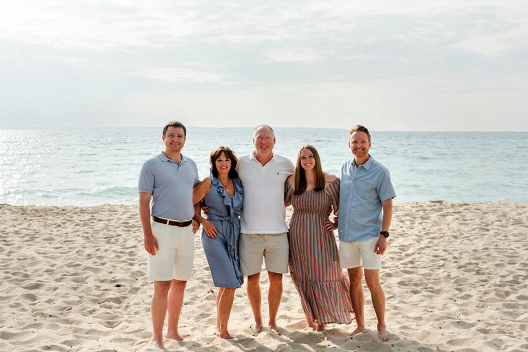 three adult children and their parents pose for family portraits on the beach.