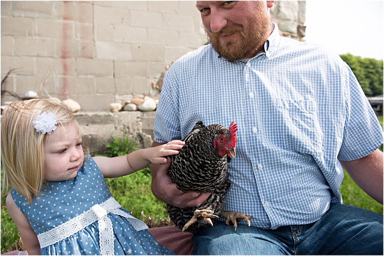a small girl petting a spotted chicken