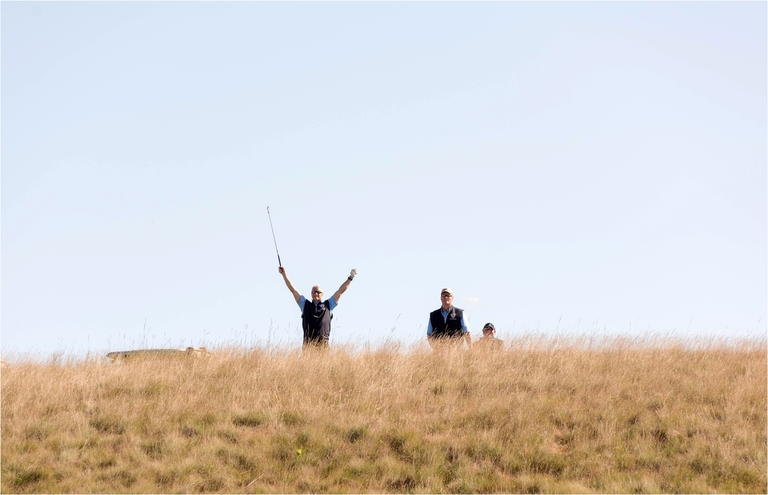 3 men on a hill. One is raising both arms