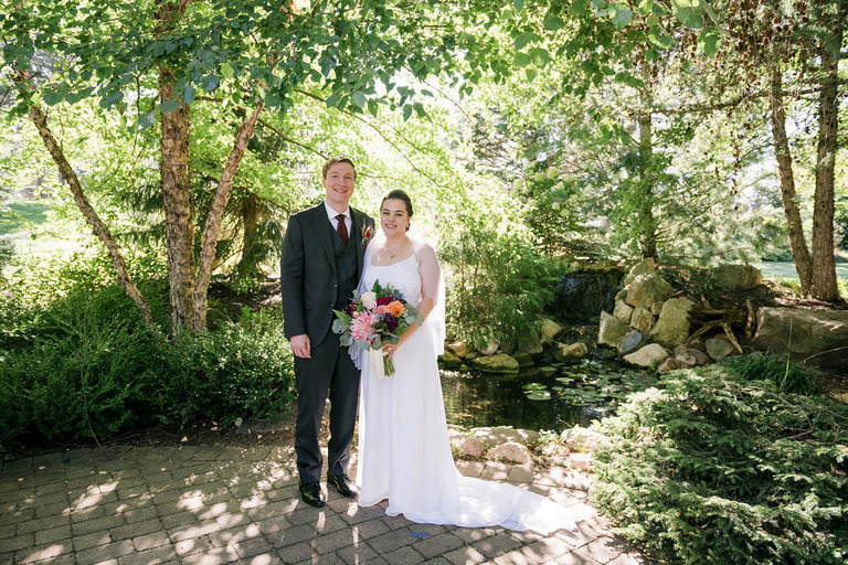 Bride wearing a white dress and groom standing in front of pond at Fox Hill Event Center