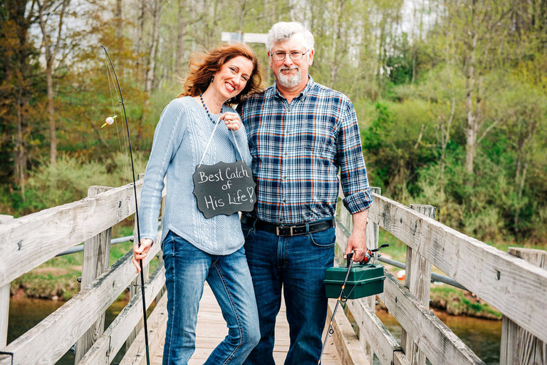 an engaged couple holding a chalkboard sign on a suspension bridge over the Manistee River