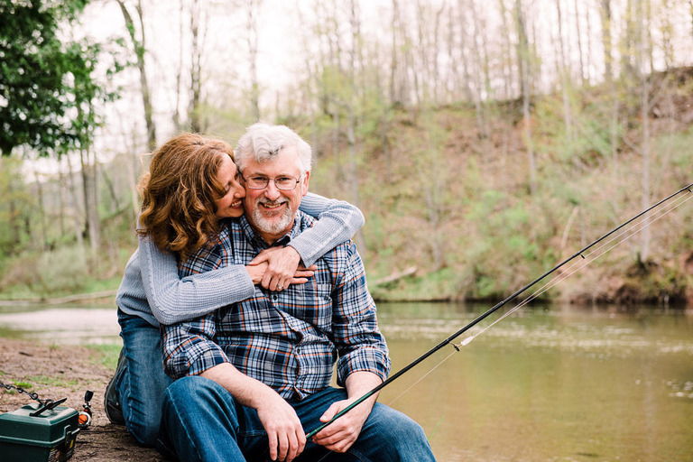 a couple embracing while looking at the camera on the bank of the Manistee River