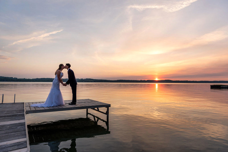 a married couple kisses on a dock in Elk Lake at sunset