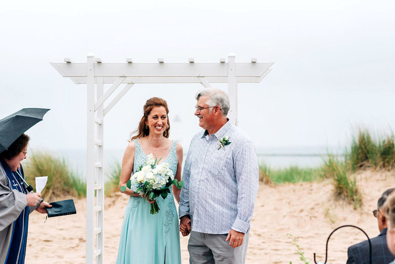 a wedding couple during the ceremony on frankfort beach. she is wearing a seafoam blue dress.