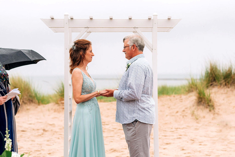 a wedding couple during the ceremony on frankfort beach. she is wearing a seafoam blue dress