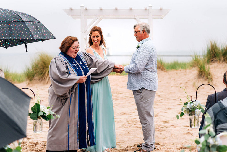 a wedding couple during the ceremony on frankfort beach. she is wearing a seafoam blue dress. Priestess is holding their hands.