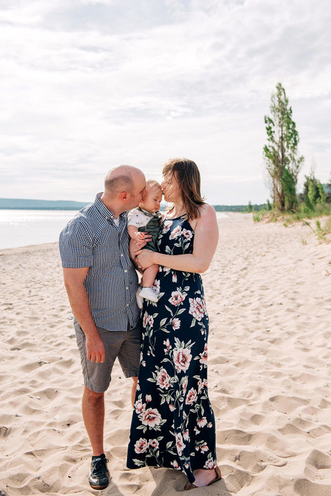 Mom and Dad kissing baby on beach at Glen Haven