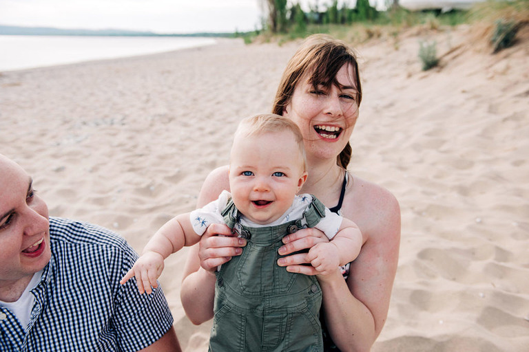a mom holds a smiling baby on the beach in Glen Haven MI