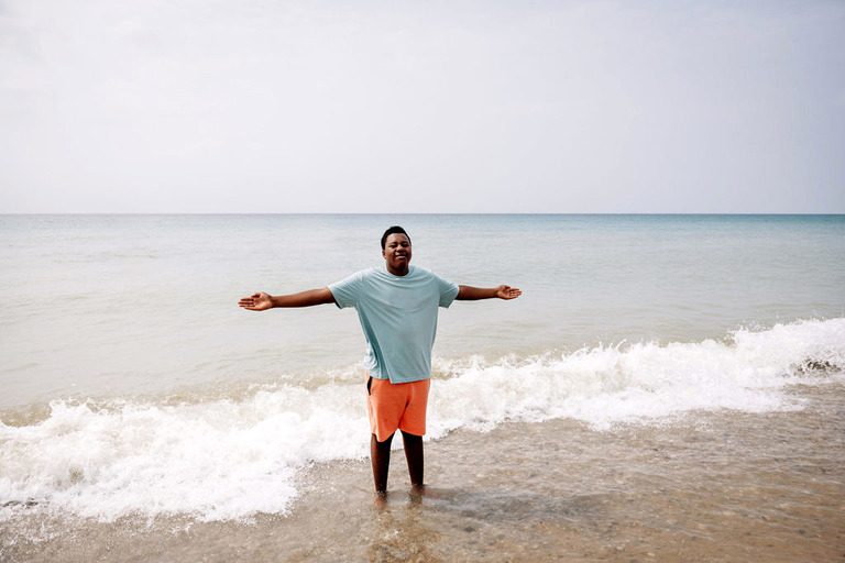 a teen boy stands in lake michigan with his arms outstretched