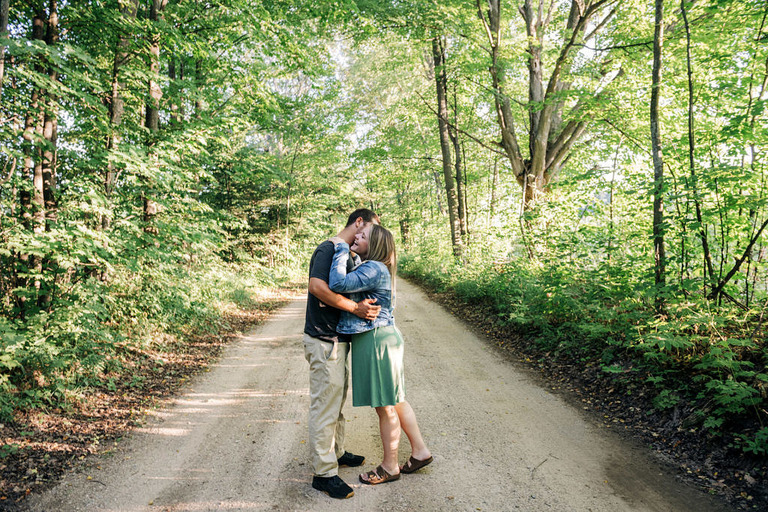 a couple embraces on a tree covered dirt road in aracadia mi