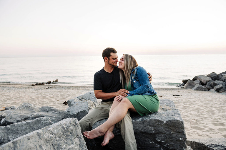 a couple embraces on the rocks at sunset on Arcadia beach mi