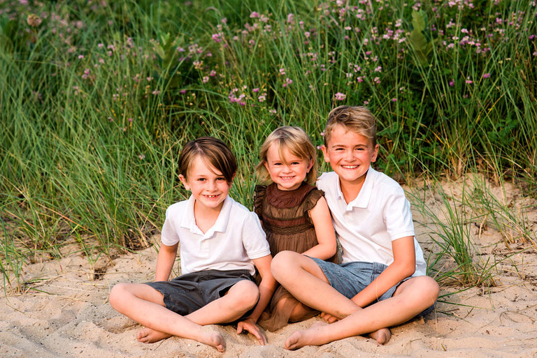 three kids sit on the sand at crystal lake beach mi