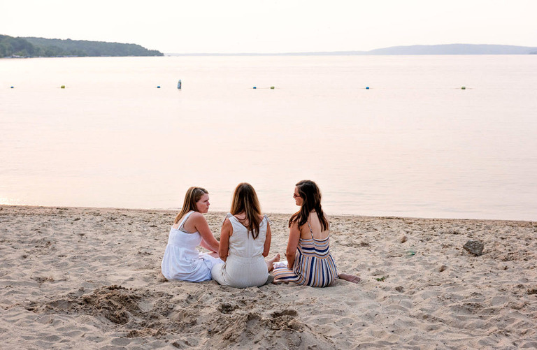 three woman sit in the sand at crystal lake mi