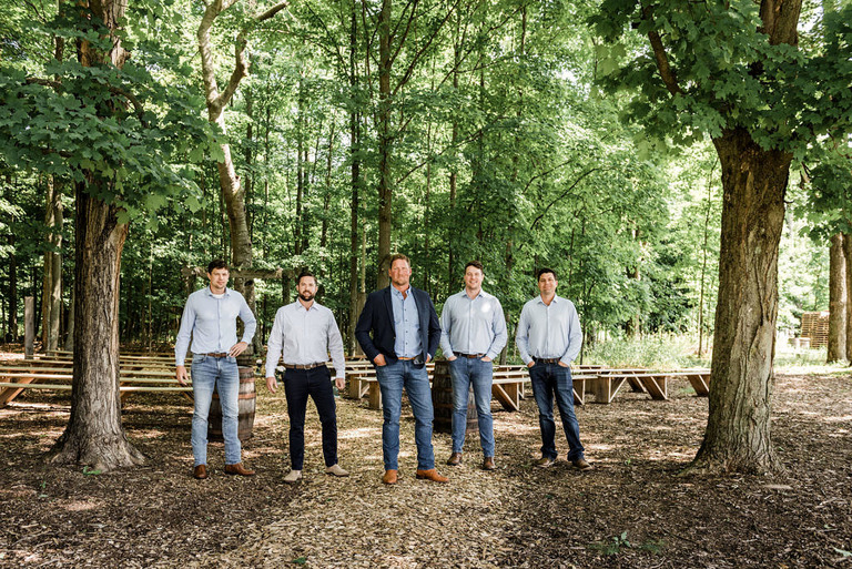 groomsmen stand in the woods at Iron Fish Distillery