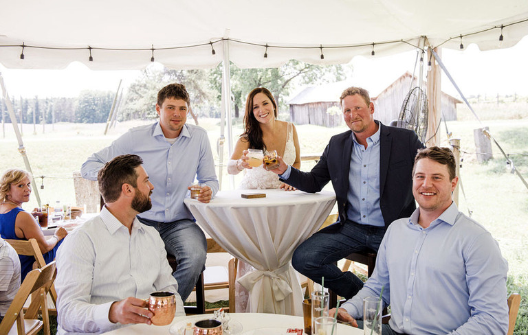 wedding party under tent saying cheers at Iron Fish Distillery