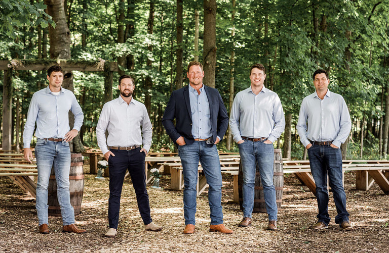 a closer photo of groomsmen wearing jeans stand in the woods at Iron Fish Distillery