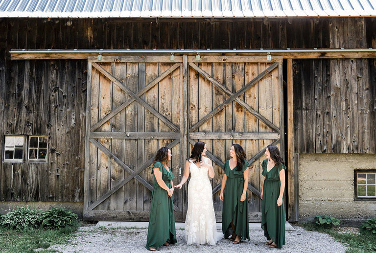 a bride in a lace dress surrounded by her bridesmaids in green dresses at Iron Fish Distillery