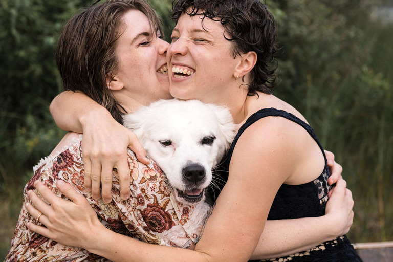 two women hug with thier white dog inbetween
