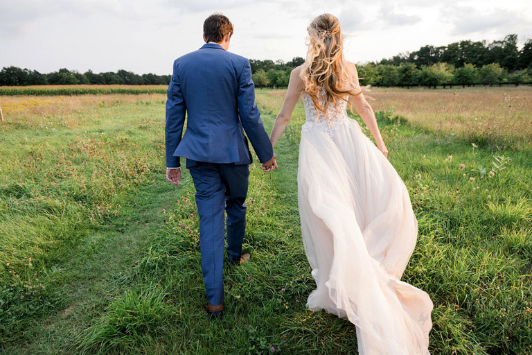 a newlywed couple walks into a field holding hands
