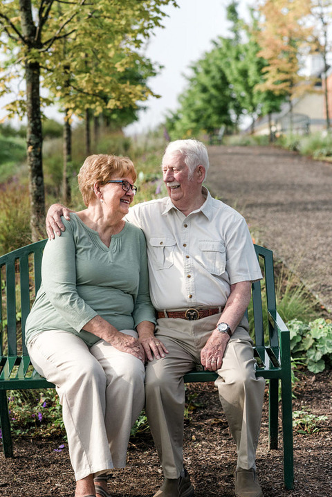 a senior couple snuggles on a park bench