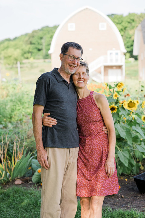 a couple hugs in front of sunflowers and the historic barn