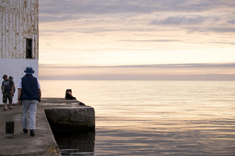 a couple sits on the edge of frankfort lighthouse at sunset