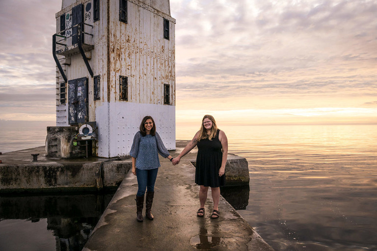 a couple holds hands at the lighthouse in frankfort, mi