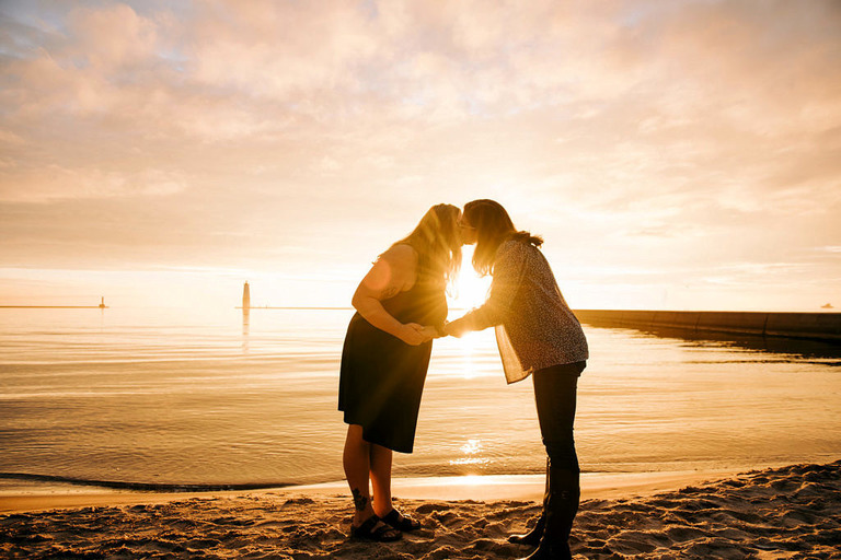 a newly engaged couple kisses on the beach in Frankfort, MI