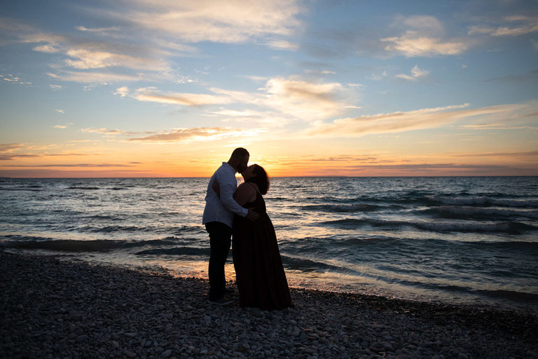an engaged couple kissing on the beach in silhouette