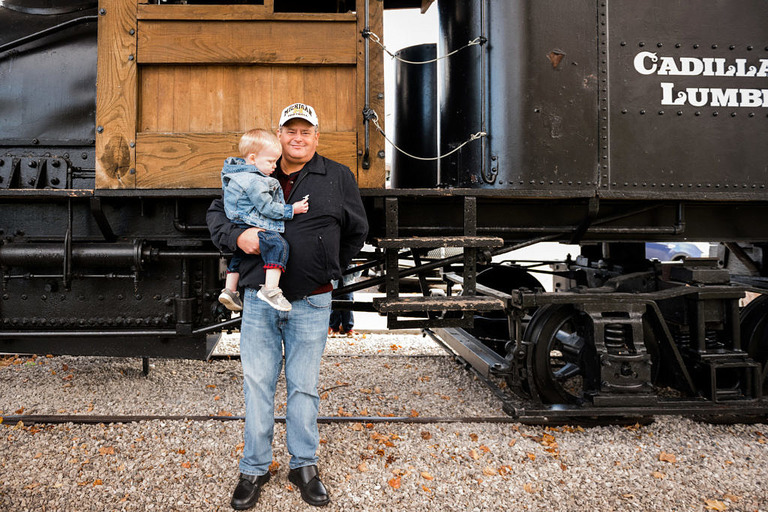 a man holding a boy in front of the train at old train depot