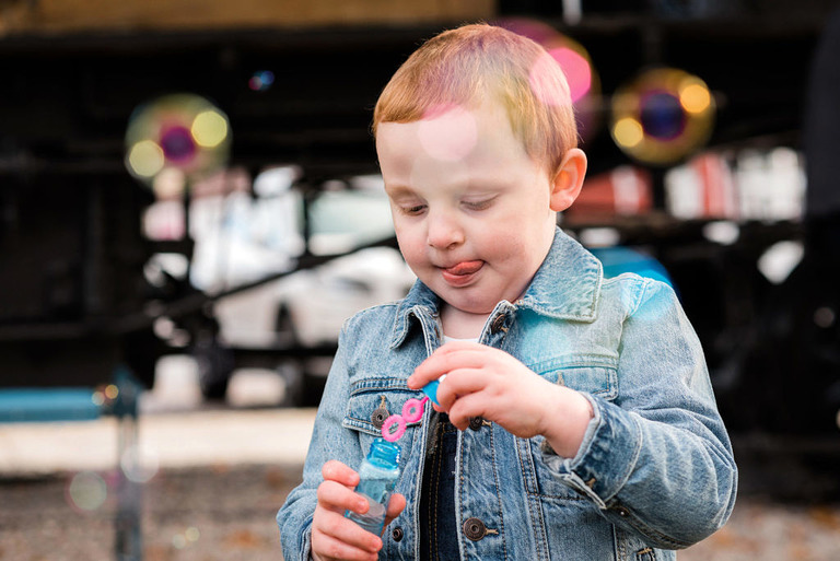 a boy in a jean jacket blows bubbles at the cadillac commons