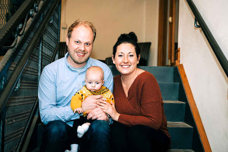 a couple and their baby on the steps inside building fifty at village commons