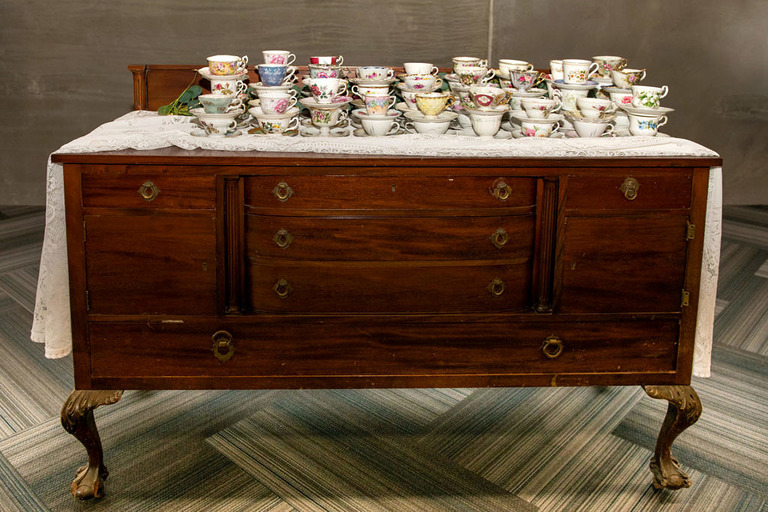 a vintage brown sideboard stacked with antique tea cups