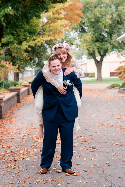 a bride in a vintage wedding dress gets a piggy back ride from her husband