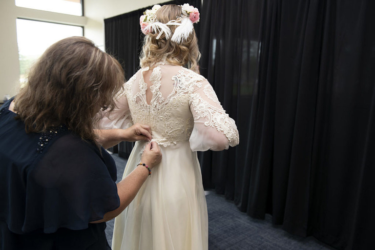 mom helps bride with buttons on the back of her wedding dress
