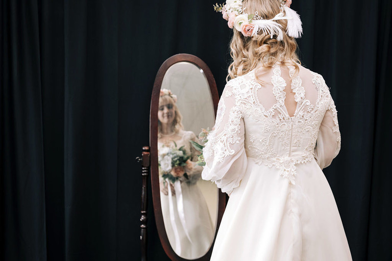 bride in vintage wedding dress looks into mirror