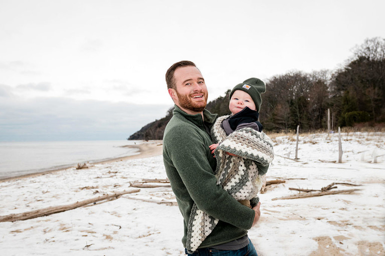  a dad in green holds his baby who is wearing a Carhartt hat 