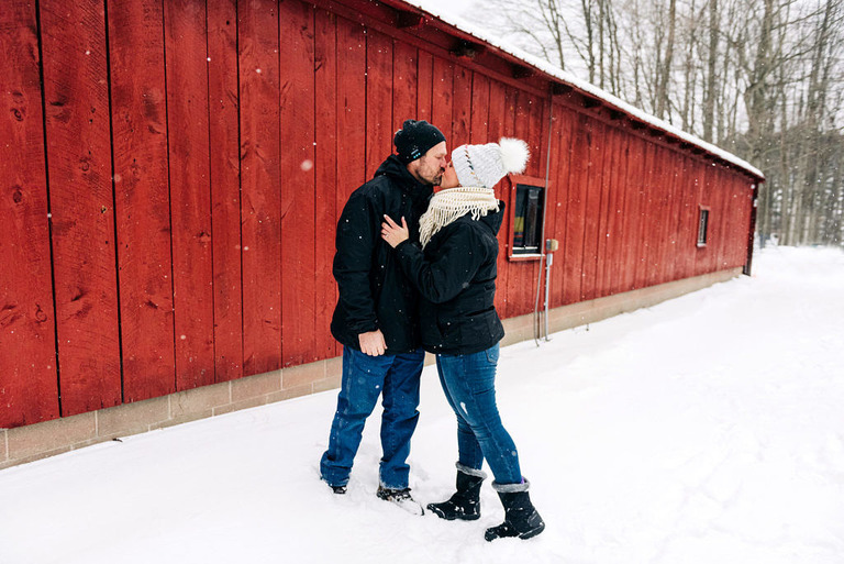 a newly engaged couple kiss outside a red barn