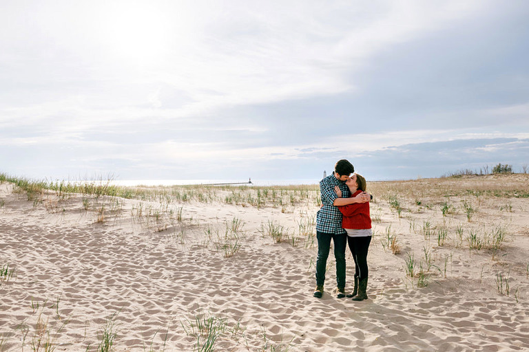 an egagement couple embraces on the dunes at Elberta beach