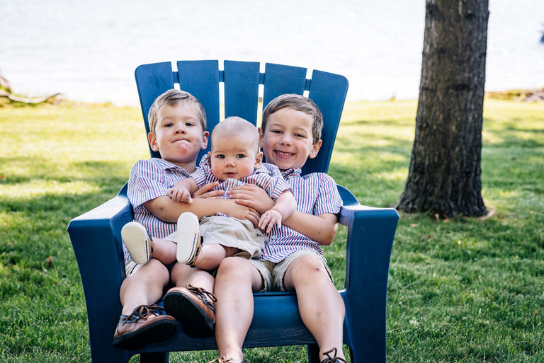 three small boys sit in an Adirondack chair on lake skegemog, MI