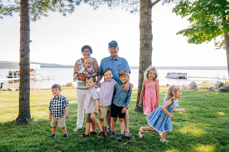grandparents standing with seven small grandchildren in front of lake skegemog