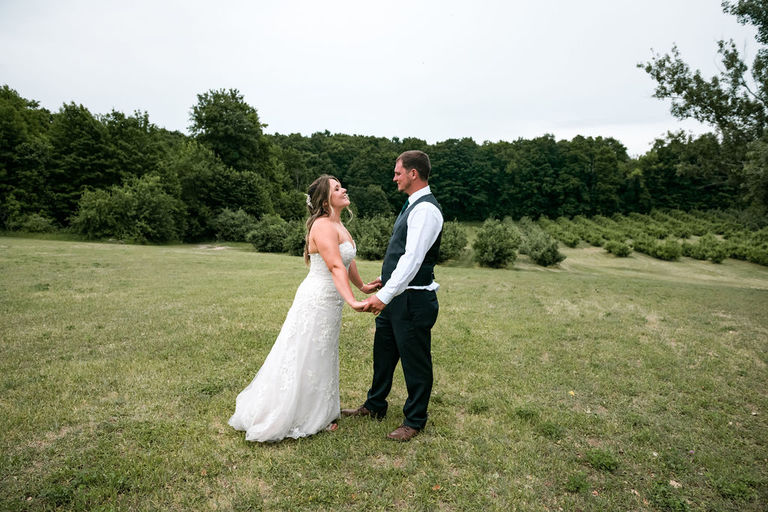 a couple stands in a green field in wedding attire