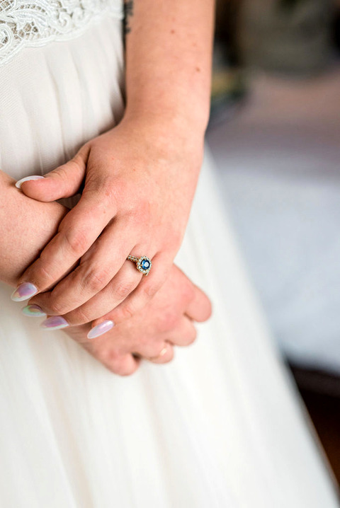a bride has her hands clasped with her sapphire engagement ring.