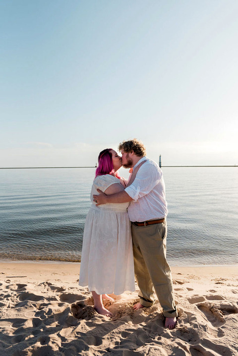 a couple in white embraces on the beach in Frankfort, Michigan.