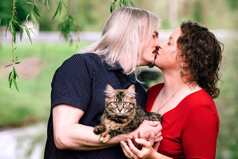 a man and a woman having engagement photos done professionally kiss while holding a striped cat