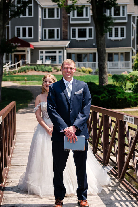 a bride stands on a bridge behind her groom about to tap him on the shoulder for a first look at the Homestead Resort.