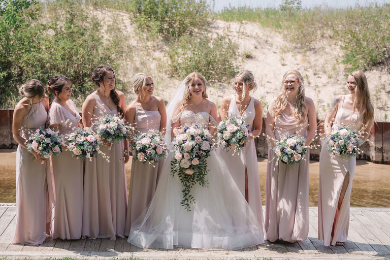 A bride is surrounded by seven bridesmaids by the river at the Homestead.