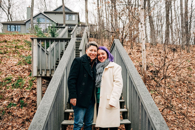 A couple stands at the bottom of a long stair case cheek to cheek smiling at the camera for engagement photos in Traverse City.