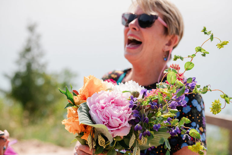 a woman laughs as she holds peonies and cottage flowers for a wedding at sleeping bear dunes.